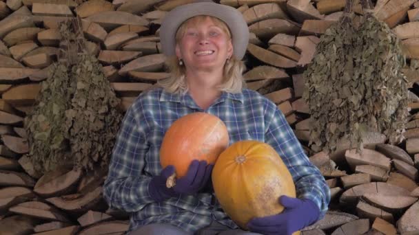 Gelukkige vrouw op een achtergrond van gestapelde brandhout bedrijf In haar Hand rijpe pompoen — Stockvideo
