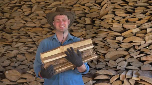 Retrato de um homem com um chapéu de cowboy em um armazém segurando um monte de lenha — Vídeo de Stock