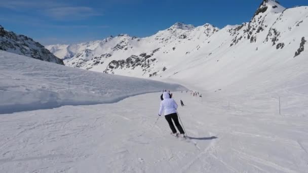 在运动的后退视图中, 滑雪者在山地度假胜地滑行下坡 — 图库视频影像