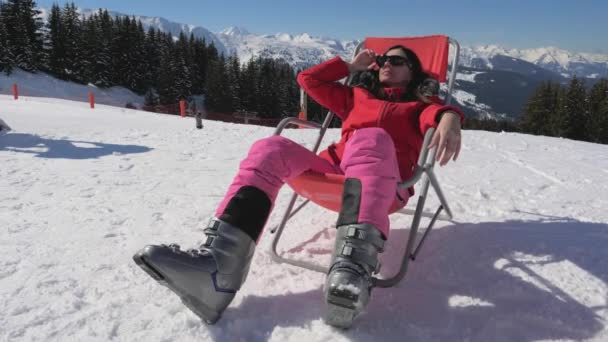 Mujer sentada en una tumbona en las montañas en invierno disfrutando del clima soleado — Vídeo de stock