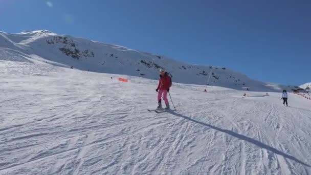 Skifahrer fahren an einem sonnigen Wintertag die Skipiste entlang des Berges hinunter — Stockvideo