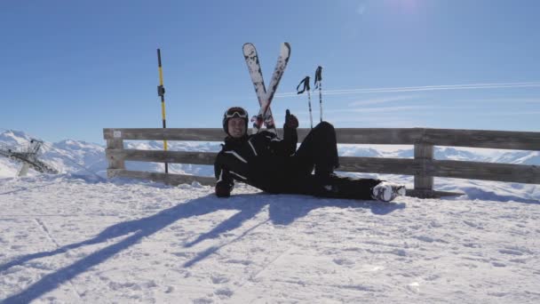 Au sommet de la montagne, le skieur repose sur la neige montrant des gestes OK et pouce en l'air — Video