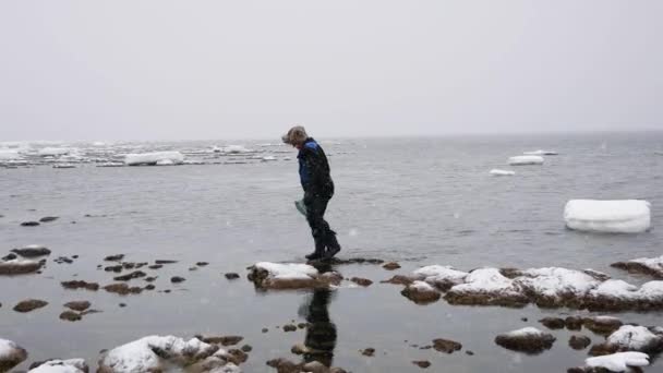 Ψαράς με ένα δικτυωτό περιπάτους κατά μήκος της παραλίας στο χειμώνα και συλλέγει λιχουδιές — Αρχείο Βίντεο