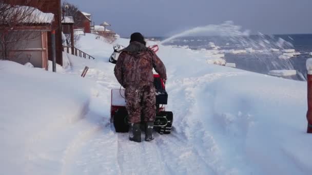 Человек очищает снежную машину от снега зимой — стоковое видео