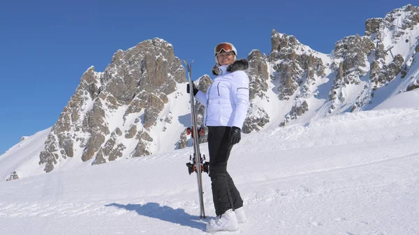 Kadın kayakçı kayaklar tutan bir dağ tarafında duruyor