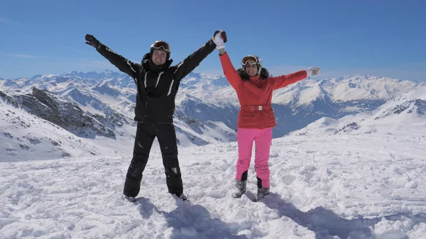 Mutlu kayakçı çift dağ tepe üzerinde duruyor ve ellerini yükselir