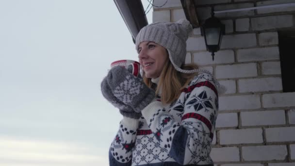 Femme se tient sur la véranda en hiver en pull et boit une tasse de café — Video