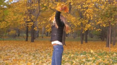 Altın sarı yapraklar tutan neşeli kadın sonbahar parkta geri dönüyor