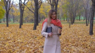 Bayan Sonbahar Park üzerinde bir klasör ya da bir dizüstü bilgisayar ve kahve tutarak yürür