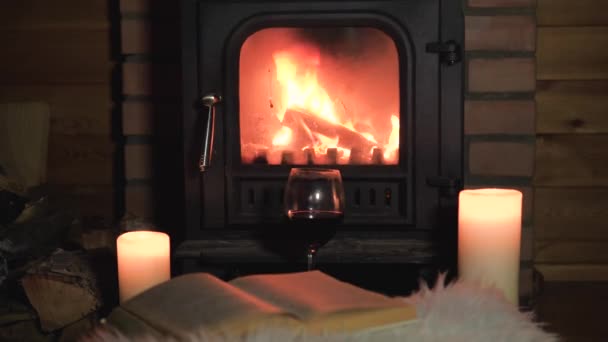 Şöminede yanan yakın alev yanan mumlar ve açık bir kitap yatıyor — Stok video