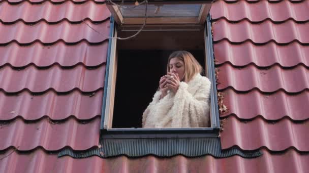 Γυναίκα απολαμβάνοντας κοιτάζοντας έξω από το παράθυρο οροφής του σπιτιού και ποτά καφέ το πρωί — Αρχείο Βίντεο