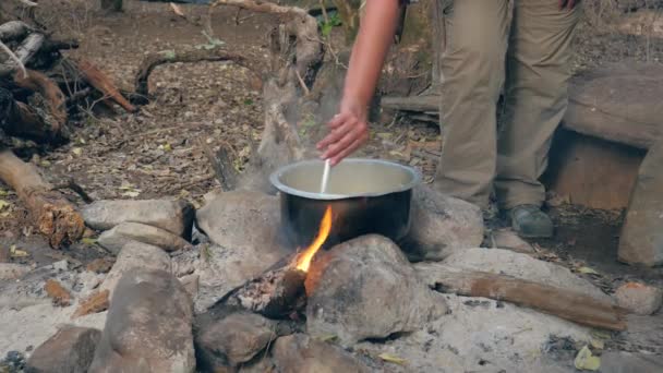 Touriste main mélange les pâtes avec une cuillère dans le pot sur le feu dans un camp — Video