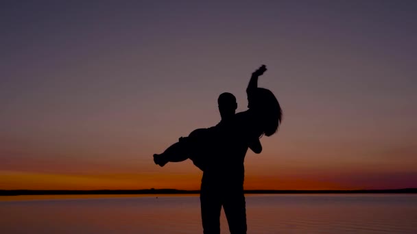 Sylwetka człowieka trzymając kobietę i krąży jej o zachodzie słońca nad morzem — Wideo stockowe