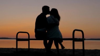 Sevgi dolu çift A üzerinde oturan bir kucaklama plaj tezgah ve güneşin batışını