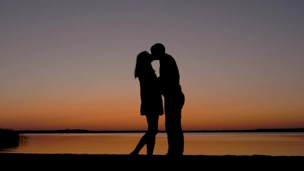 Sziluettjét pár férfi és nő megcsókolta a romantikus naplemente a tenger parton — Stock videók