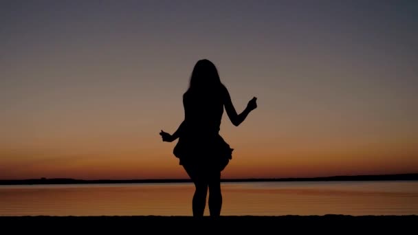 Σιλουέτα του μια γυναίκα που χορεύει σέξι στο ηλιοβασίλεμα δίπλα στη θάλασσα — Αρχείο Βίντεο