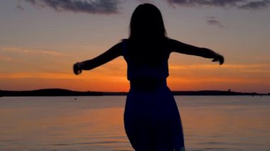 Sahile kadar kollarını yükselterek ve etrafında dönen batımında mutlu kadın