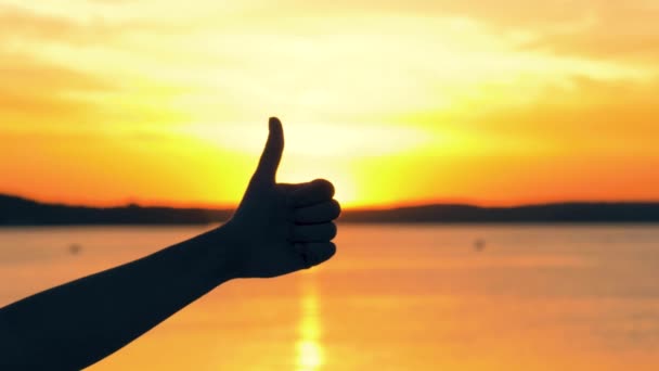 Primer plano de la silueta de mano muestra el gesto de pulgar hacia arriba en los rayos de sol al atardecer de oro — Vídeo de stock