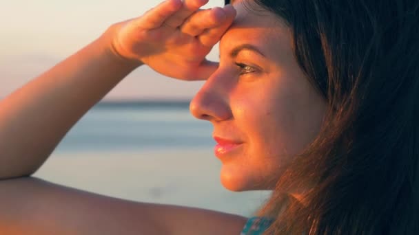 Mujer mirando al mar durante la puesta del sol cubierta del sol con su mano — Vídeo de stock