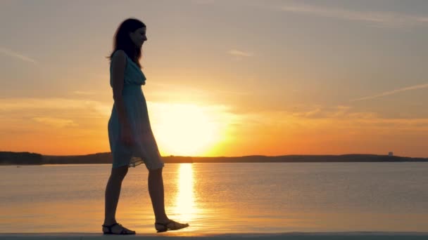 Linda mulher em um vestido andando ao longo da praia ao pôr do sol em uma noite de verão — Vídeo de Stock