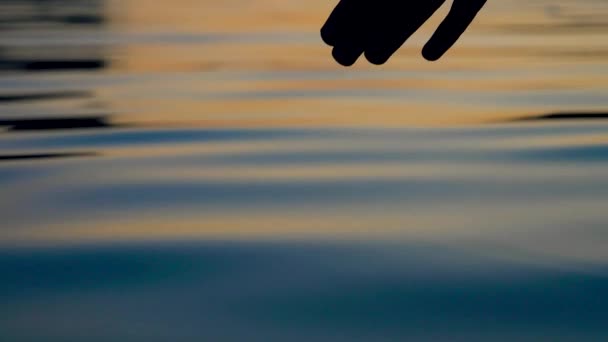 Аккуратно касается поверхности воды кончиками пальцев в золотом закате — стоковое видео