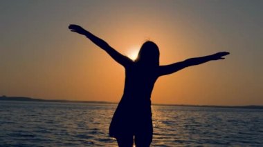 Genç kadın silüeti ellerini yukarı ve yan günbatımında denizde kaldırdı