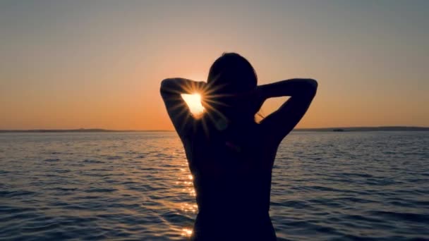 Voltar vista das mulheres na costa corrigir seu cabelo nos raios do pôr do sol — Vídeo de Stock