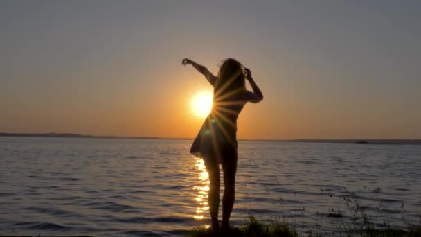 Silhuetten av en lycklig kvinna som vackert och graciöst dansar vid solnedgången på havet — Stockvideo