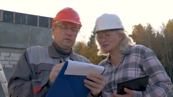 Trabajadores de la construcción en casco discuten construcción según proyecto de plan — Vídeo de stock