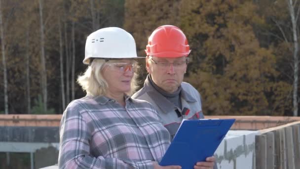 Rolig byggare i hjälmar titt på planen då undra och skakar på huvudet — Stockvideo