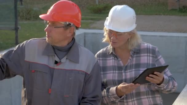 Construtor e cliente no capacete discutem a construção de acordo com o projeto do plano — Vídeo de Stock