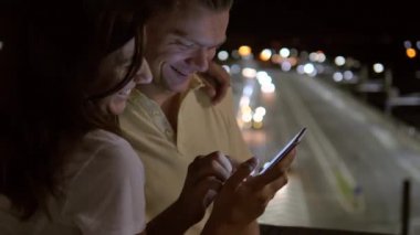 Mutlu çift akşam sokakta Smartphone vasıl birlikte seyir gülümseyen