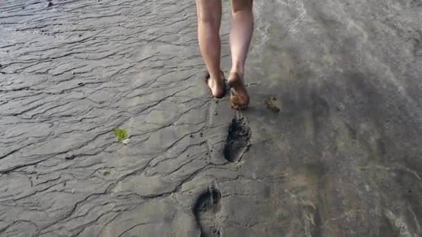 Ноги пожилого белого человека едва идут по берегу, оставляя следы на черном песке — стоковое видео