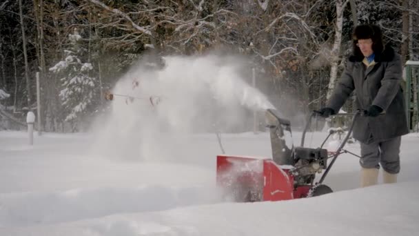L'homme nettoie la neige avec une lueur de neige sur le fond de la forêt en hiver — Video