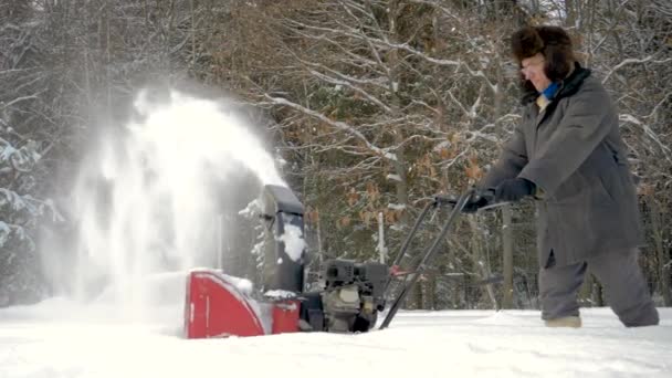 Trabalhador limpa a estrada da neve com fluxo de neve no fundo da floresta no inverno — Vídeo de Stock