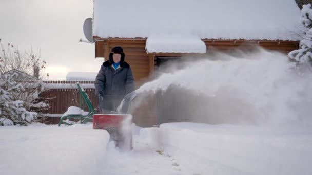 L'homme nettoie la neige avec neige souffle fond de maison en bois en hiver — Video