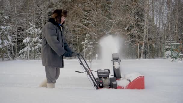 El hombre limpia el camino de la nieve con el resplandor de nieve en el fondo del bosque en invierno — Vídeo de stock