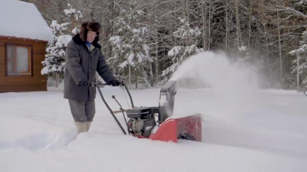 Άνθρωπος χιόνι με χιόνι Άροτρο φόντου από ξύλινο σπίτι καθαρίζει το χειμώνα — Αρχείο Βίντεο