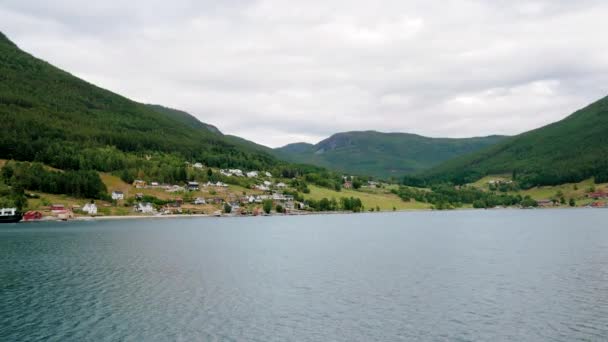 Navegue na bela baía de fiordes noruegueses contra as colinas com a aldeia — Vídeo de Stock