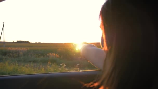 Pretty Young Caucasian Woman In Car And Hand Playing In The Air At Sunset Rays — Stok Video