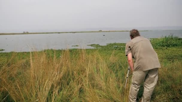 Fotograf přírodovědec fotografuje s kamerou na stativu fotografii divokého Hippo v jezeře — Stock video