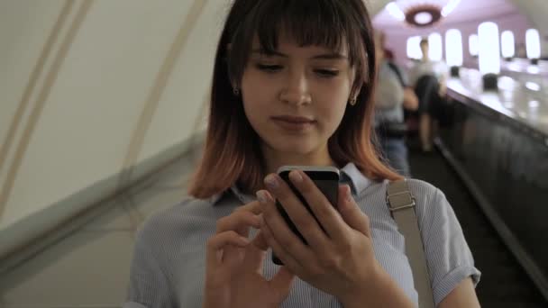 Atractiva mujer monta escaleras mecánicas hasta el metro usando un teléfono inteligente — Vídeos de Stock