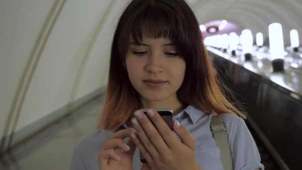 Mulher feliz cavalga escada rolante até o metrô usando um smartphone — Vídeo de Stock