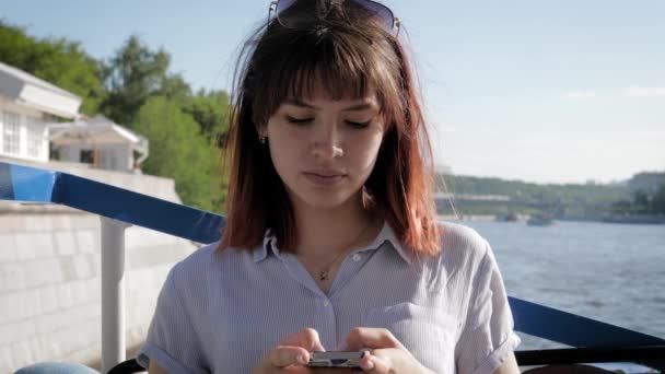 Jovem mulher caucasiana atraente usa aplicativos de smartphones no fundo do rio — Vídeo de Stock