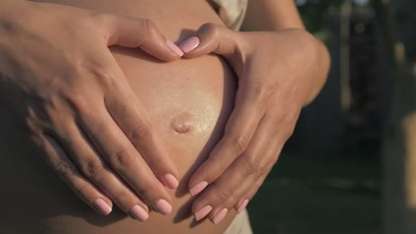 Schwangere macht im Licht des Sonnenuntergangs mit den Händen ein Herz auf dem Bauch — Stockvideo