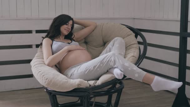 Enceinte caucasien femme assis sur un relax chaise et caressant son estomac — Video