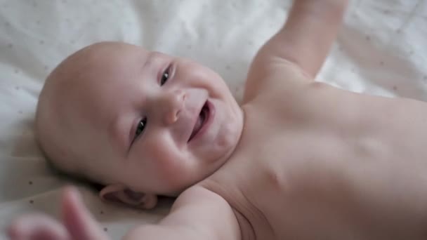 Закрыть портрет забавного маленького младенца, играючи лежащего в белой кровати — стоковое видео