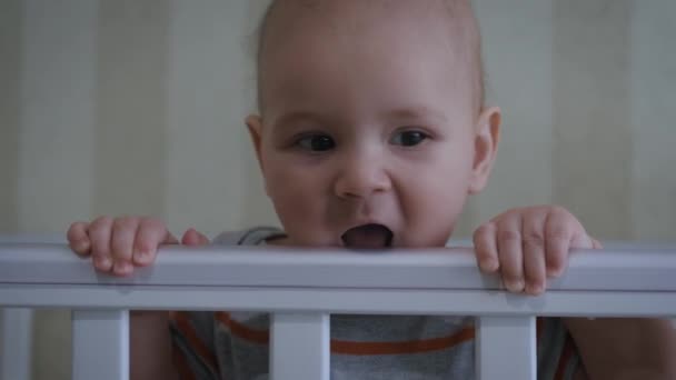 Vrolijke kleine baby knabbels op de Railing van zijn wieg en glimlacht — Stockvideo