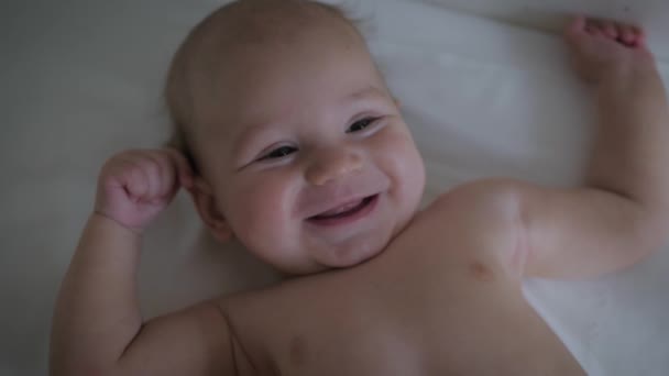 Закройте портрет забавного маленького младенца, играючи лежащего в кровати — стоковое видео
