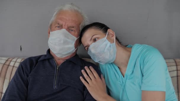 Кавказька жінка у медичній масці обнімає літнього чоловіка, який підтримує і дбає про нього — стокове відео
